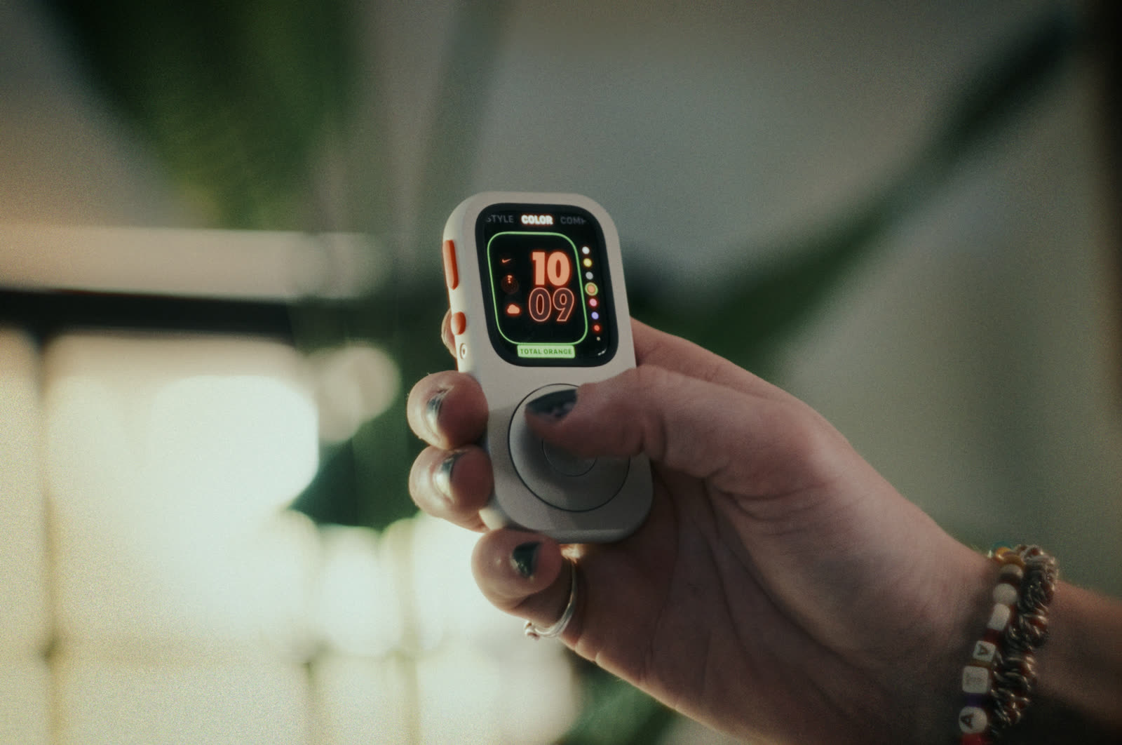 円形のホイールの上にカラフルなApple Watchの文字盤を表示した、前面カメラ付きの銀色のRePodを手に持つ手